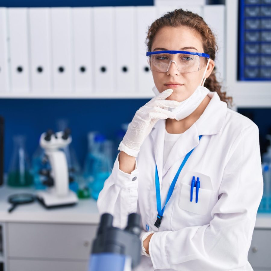 Young caucasian woman working at scientist laboratory smiling looking confident at the camera with crossed arms and hand on chin. thinking positive.
